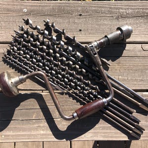 May include: A vintage hand drill with a wooden handle and a set of drill bits. The drill bits are made of metal and have different sizes. The drill is a useful tool for woodworking and other DIY projects.