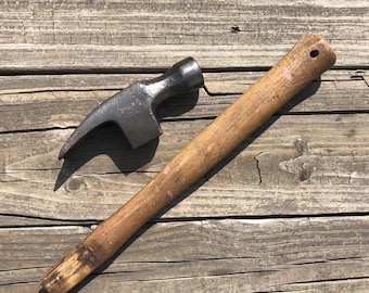 May include: A vintage hammer with a wooden handle. The hammer head is black and has a curved claw. The handle is brown and has a slight pink tint.
