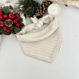 May include: A white knitted bandana with a cable knit pattern and a small label that says "Jane & June".