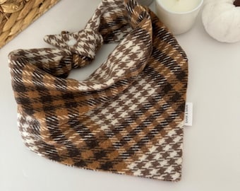 May include: A brown and white plaid bandana with a houndstooth pattern. The bandana is tied in a knot and has a small white tag with the text "BARK & BAHN" on it.