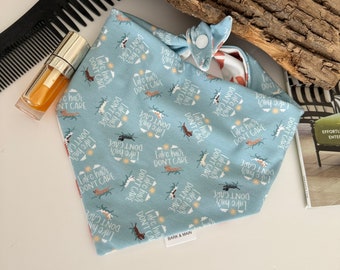 Puede incluir: Un bandana azul con un estampado de perro blanco y marrón. El bandana tiene el texto "Lake hair, don't care" repetido en todo el estampado. El bandana tiene un cierre a presión.