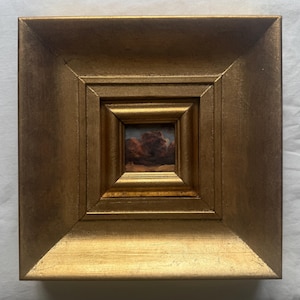 Peut inclure: Une petite peinture carrée représentant un paysage sombre et mélancolique aux tons rouge foncé et marron, encadrée dans un large cadre doré orné avec un profil biseauté à gradins qui attire le regard vers l'œuvre centrale.