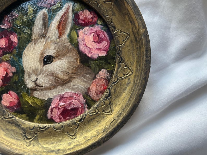 May include: A white rabbit with pink eyes surrounded by pink roses in a gold frame.