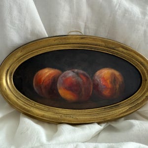 Peut inclure: Peinture à l'huile ovale encadrée d'or représentant trois pêches. Les pêches sont peintes dans des tons de rouge, d'orange et de jaune sur un fond sombre. Le cadre a une finition dorée vieillie.