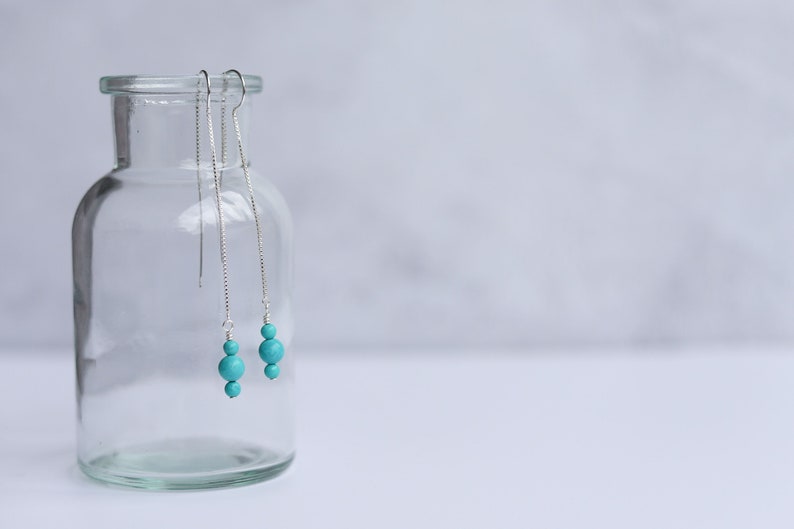 May include: A pair of turquoise dangle earrings with silver chains hanging from a glass jar.