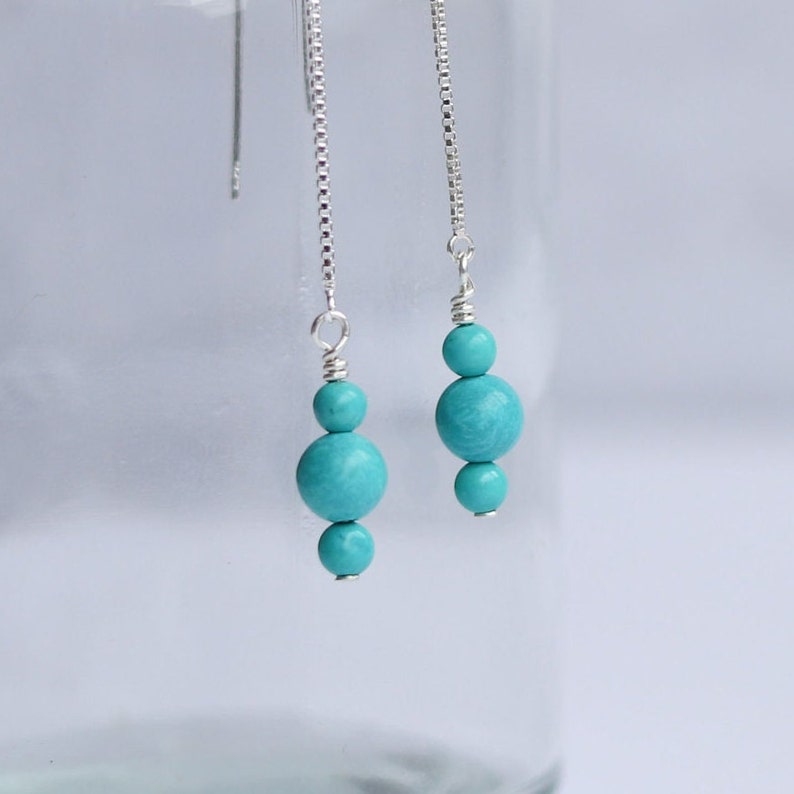 May include: A pair of turquoise gemstone dangle earrings with silver chain and beads.