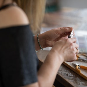 May include: A person is using jewelry making tools to create a piece of jewelry. The tools include a pair of pliers, a pair of wire cutters, and a small container of beads.