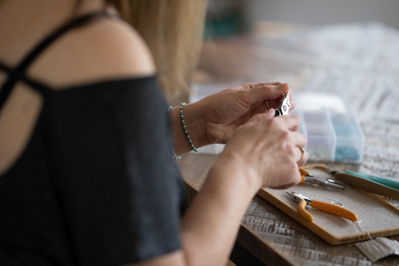May include: A person is using jewelry making tools to create a piece of jewelry. The tools include a pair of pliers, a pair of wire cutters, and a small container of beads.