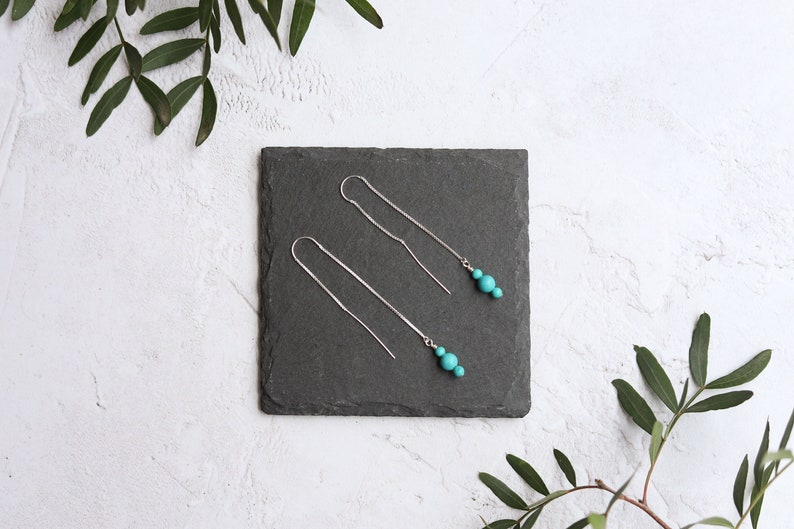 May include: A pair of silver dangle earrings with turquoise beads. The earrings are displayed on a black slate tile.
