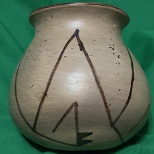 May include: A beige ceramic vase with a rounded body and a slightly flared rim. The vase features dark brown, abstract linear designs on its surface. The vase has a speckled texture and a dark brown rim.