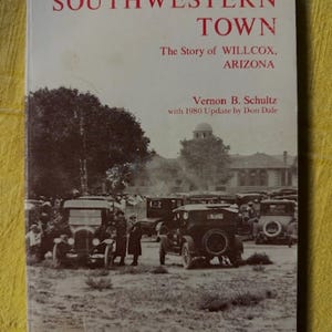 May include: A book titled Southwestern Town: The Story of Willcox, Arizona by Vernon B. Schultz with a 1980 update by Don Dale. The cover features a sepia-toned historical photograph of vintage automobiles and people in a town square setting.