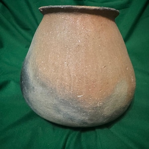 以下が含まれることがあります： 丸みを帯びたボディとわずかに広がった縁を持つ、手作りの陶器の壺。茶色、タン、グレーの色合いで、自然でアースカラーの配色です。表面は質感があり、素朴で職人的な品質を示唆しています。壺は、おそらく保管または装飾目的で使用されます。