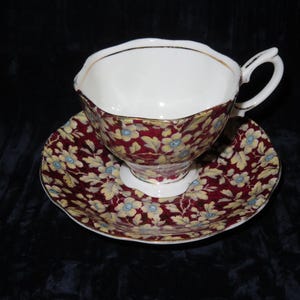 Peut inclure: Une tasse à thé et une soucoupe vintage avec un motif floral. La tasse et la soucoupe sont blanches avec un motif floral rouge et or. Les fleurs sont jaunes avec des centres bleus.