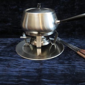 Può includere: Un set per fonduta in acciaio inossidabile, composto da una pentola con manico e coperchio neri, un supporto e un piatto. Include forchette per fonduta con punte colorate. Per servire formaggio o cioccolato fuso.