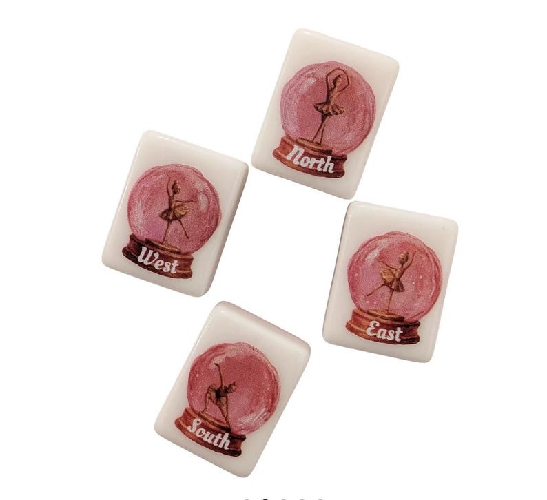 May include: Four white tiles featuring a ballerina in a pink snow globe design. Each tile is labelled with a compass direction: North, South, East, and West. The tiles are arranged in a circular pattern against a white backdrop.