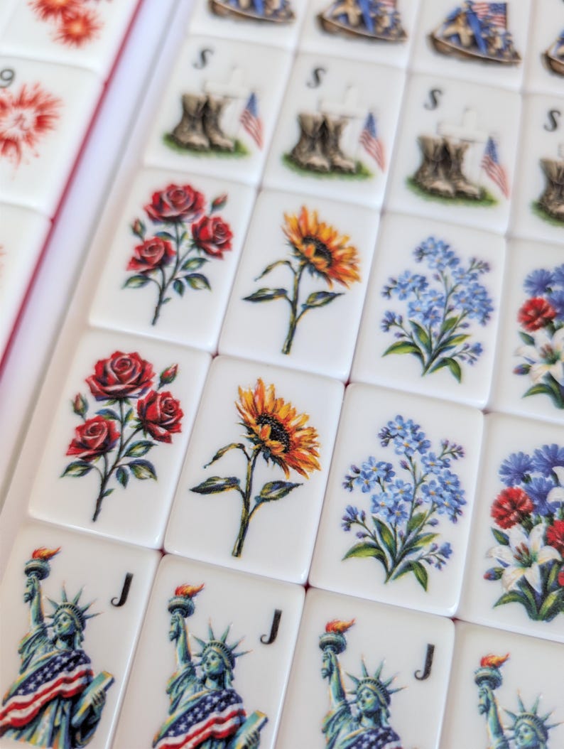 May include: A collection of rectangular white mahjong tiles featuring various printed designs including red roses, yellow sunflowers, blue forget-me-nots, the Statue of Liberty with a flag, and military boots with an American flag and the letter S.