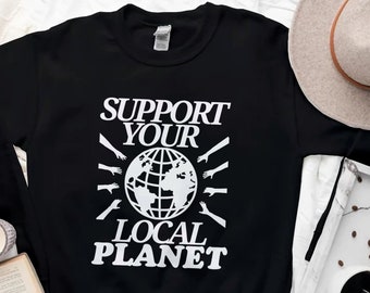Puede incluir: Sudadera negra con texto blanco que dice "Support Your Local Planet". El texto está rodeado por un gráfico de un globo terráqueo con manos que se extienden.