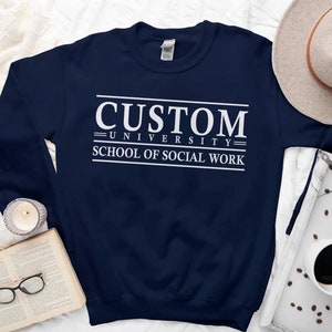 May include: A navy blue sweatshirt with white text that reads "CUSTOM UNIVERSITY SCHOOL OF SOCIAL WORK".