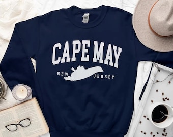 May include: Navy blue sweatshirt with white text that reads "CAPE MAY NEW JERSEY" and a white outline of the state of New Jersey.