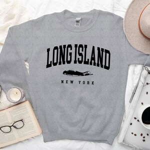 K&ouml;nnte beinhalten: Grauer Pullover mit schwarzem Text "LONG ISLAND NEW YORK" und einer Silhouette von Long Island.