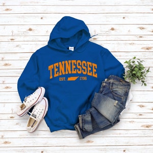May include: A royal blue hooded sweatshirt with the word "Tennessee" in orange arching over the state outline in orange. The text "EST. 1796" is below the state outline.