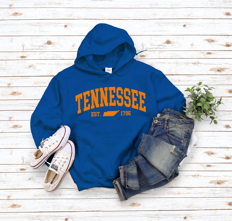 May include: A royal blue hooded sweatshirt with the word "Tennessee" in orange arching over the state outline in orange. The text "EST. 1796" is below the state outline.