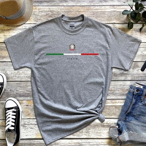 Puede incluir: Una camiseta gris con una peque&ntilde;a bandera italiana y la palabra "ITALIA" impresa en la parte delantera.