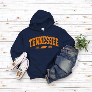 May include: A navy blue hooded sweatshirt with an orange graphic print of the state of Tennessee and the text "Tennessee Est. 1796".