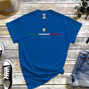 Puede incluir: Una camiseta azul real con una franja verde, blanca y roja a trav&eacute;s del pecho. La franja presenta un peque&ntilde;o emblema de la bandera italiana y la palabra "ITALIA" debajo.