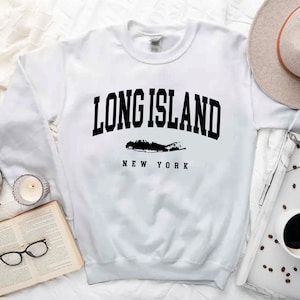 K&ouml;nnte beinhalten: Wei&szlig;er Langarm-Pullover mit schwarzem Text "LONG ISLAND NEW YORK" und einer Silhouette von Long Island.