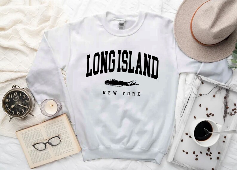 K&ouml;nnte beinhalten: Wei&szlig;er Langarm-Pullover mit schwarzem Text "LONG ISLAND NEW YORK" und einer Silhouette von Long Island.
