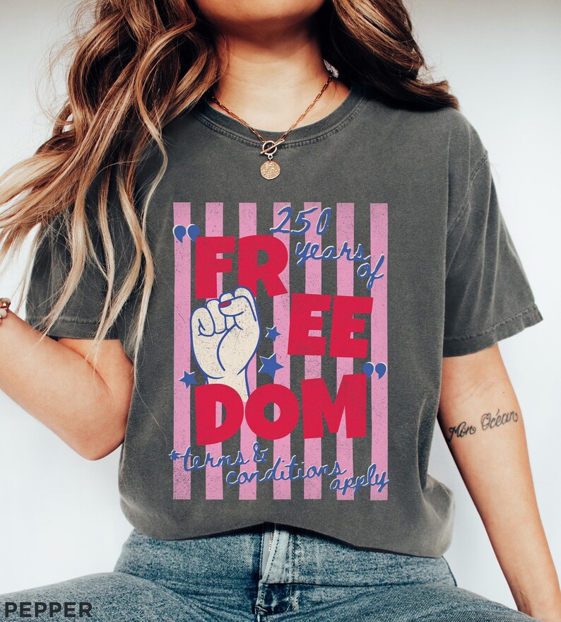 May include: Dark gray t-shirt with a graphic that reads "250 years of FREEDOM" in red letters. The design includes a raised fist, stars, and pink and white stripes. The text "*terms & conditions apply" is in blue.