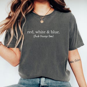 May include: Dark grey t-shirt with the text "red, white & blue. (fuck trump too)" in white. The shirt has a crew neck and short sleeves. The shirt is made of a soft material.