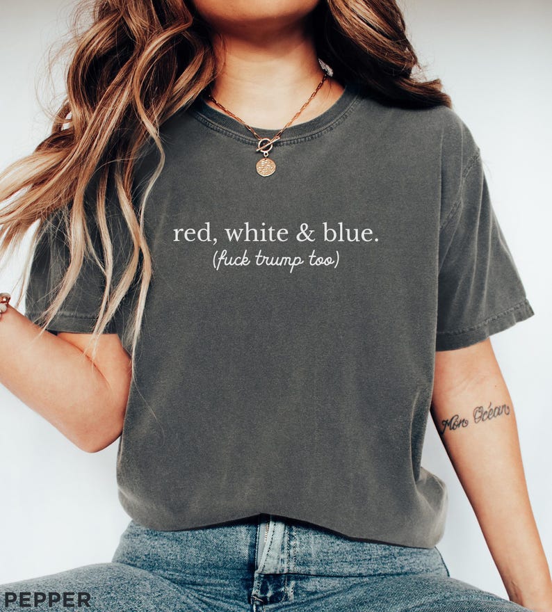 May include: Dark grey t-shirt with the text "red, white & blue. (fuck trump too)" in white. The shirt has a crew neck and short sleeves. The shirt is made of a soft material.