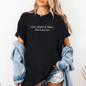 May include: Black t-shirt with the text "red, white & blue. (fuck trump too)" in white. The shirt is worn with a denim jacket and shorts. The shirt is a casual wear item.
