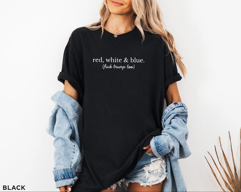 May include: Black t-shirt with the text "red, white & blue. (fuck trump too)" in white. The shirt is worn with a denim jacket and shorts. The shirt is a casual wear item.