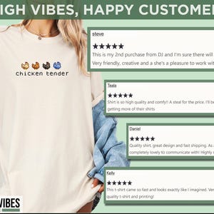 May include: A cream-coloured t-shirt with the text "chicken tender" and pixelated chicken graphics. The shirt also features the text "HIGHER VIBES SHOPPE". Customer reviews are displayed in the background.