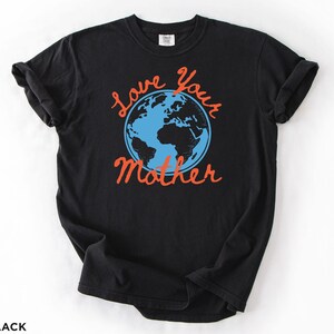 May include: Black t-shirt featuring the phrase "Love Your Mother" in orange script, surrounding a blue and black illustration of the Earth. The shirt has short sleeves and is made of a soft material.