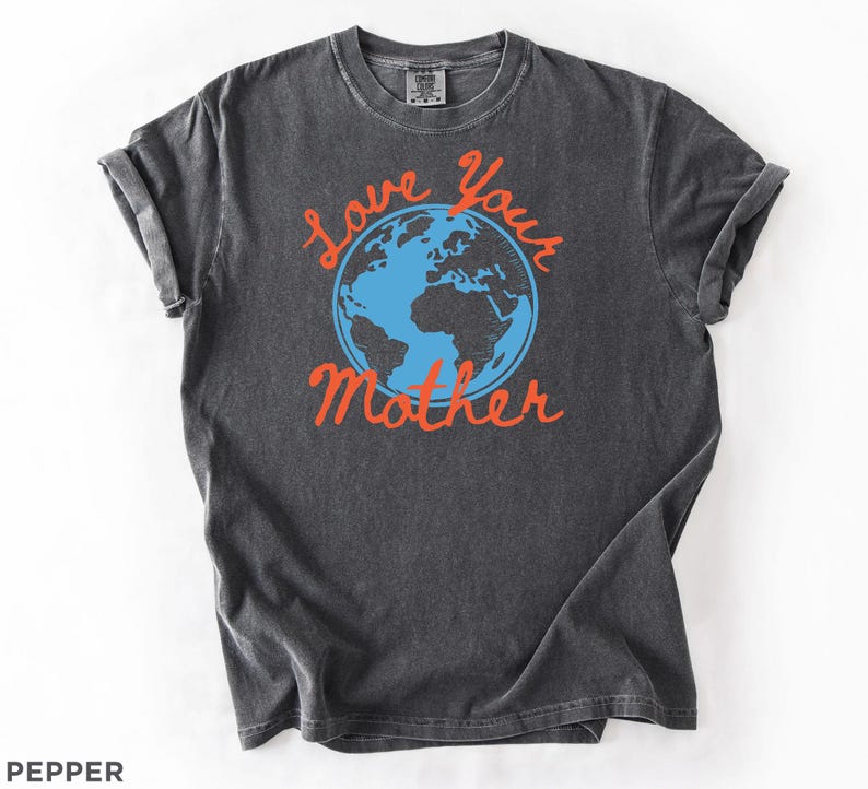 May include: A dark grey t-shirt with rolled sleeves. The shirt displays a blue and orange graphic of the Earth with the words "Love Your Mother" in orange script. The shirt is made of a soft, comfortable material.