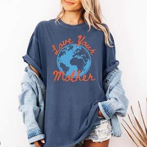 May include: A navy blue t-shirt featuring the phrase "Love Your Mother" in orange script, surrounding a blue and orange globe. The shirt is part of a denim collection.