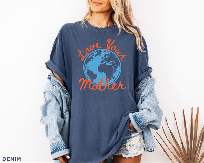 May include: A navy blue t-shirt featuring the phrase "Love Your Mother" in orange script, surrounding a blue and orange globe. The shirt is part of a denim collection.