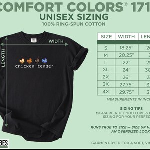 May include: Black Comfort Colors t-shirt with the text "chicken tender" and four pixelated chickens. The shirt includes a size chart with measurements in inches, ranging from 46.35 cm width and 67.56 cm length to 75.57 cm width and 85.09 cm length.