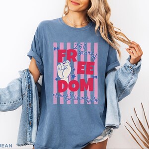 May include: Blue jean t-shirt with a graphic that reads "250 years of FREEDOM" in red and white. The graphic includes a raised fist and stars, with the text "terms & conditions apply" below.
