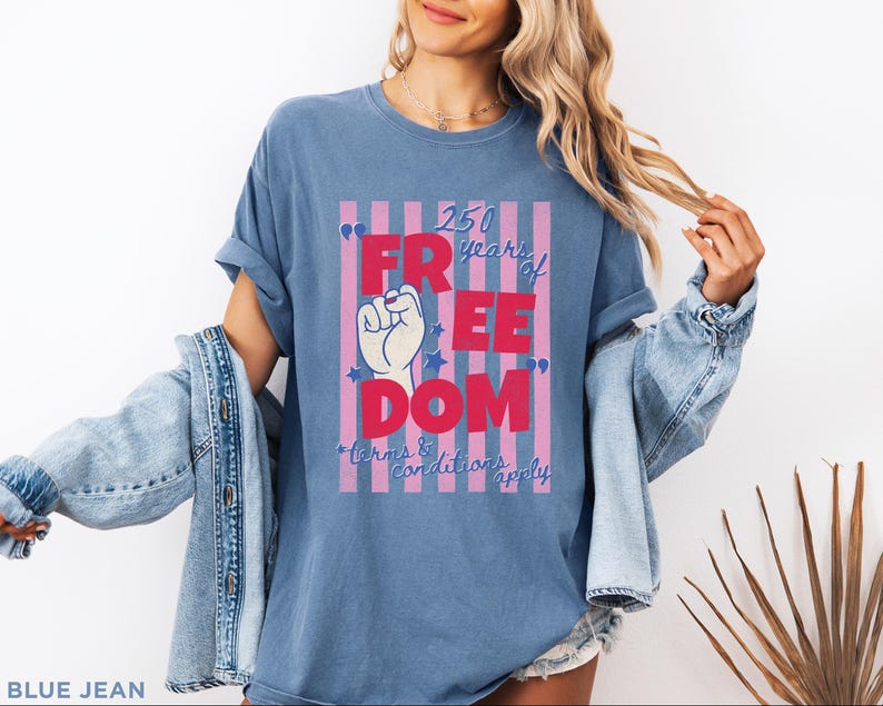 May include: Blue jean t-shirt with a graphic that reads "250 years of FREEDOM" in red and white. The graphic includes a raised fist and stars, with the text "terms & conditions apply" below.