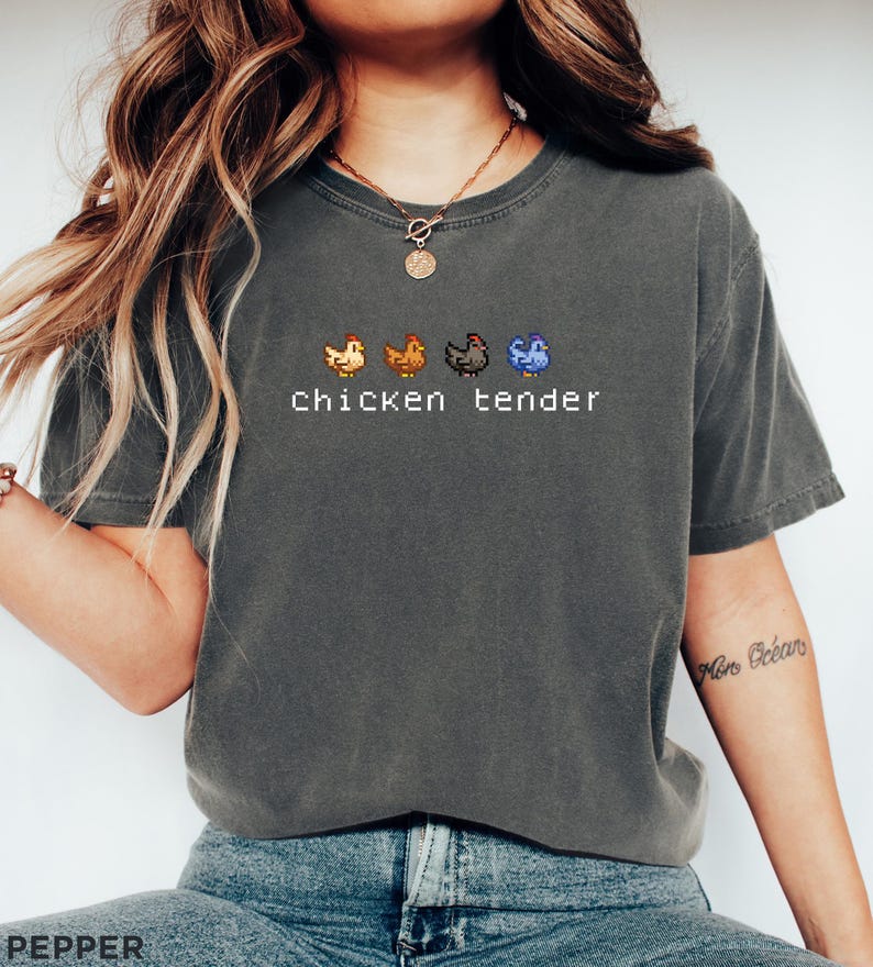 May include: Dark grey t-shirt featuring the text "Chicken tender" and four pixelated chicken illustrations in orange, brown, black, and blue. The shirt has a crew neck and short sleeves.