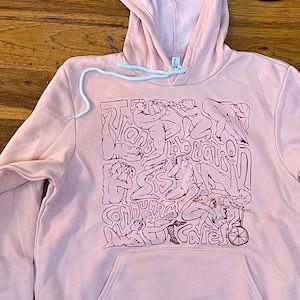 Könnte beinhalten: Ein rosa Kapuzenpullover mit einem grafischen Druck eines Designs mit mehreren Figuren und dem Text "The Body Is Sacred".