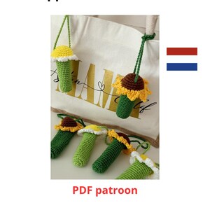 May include: Crocheted lip balm holders in various colors, including green, yellow, and brown, shaped like flowers. The holders are hanging from a white tote bag. The text "Lippenbalsem houder" and "PDF patroon" are visible.