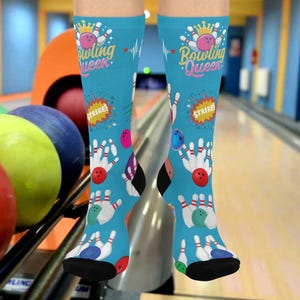 May include: A pair of light blue socks with a bowling theme. The socks feature the text "Bowling Queen" with a crown and bowling pin graphics. Additional graphics include bowling pins, bowling balls, and the word "STRIKE!"