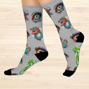 May include: Gray socks with a repeating pattern of colorful dragons and stylized eyes. The dragons are in shades of red, teal, and green, with black heels and toes. The socks are on a light wood background.