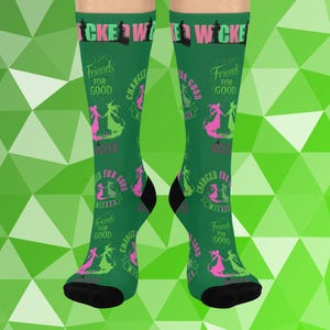 May include: Green socks with black heels and toes, featuring the text "WICKED" and "Friends for Good". The socks have a repeating pattern of two witch silhouettes in pink and green, with the words "CHANGED" and "WICKED".